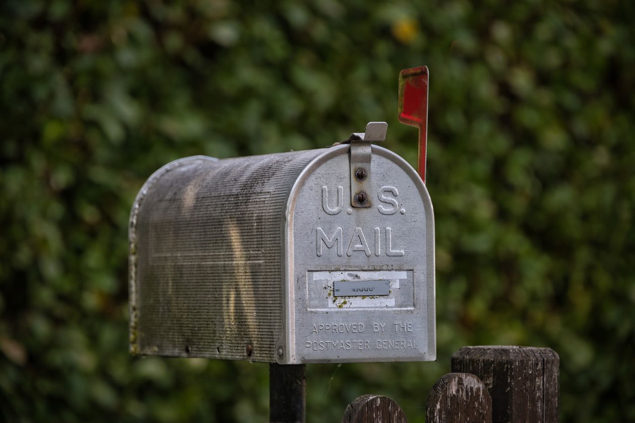 services-02 A traditional U.S. mailbox with red flag against a lush green blurred background.